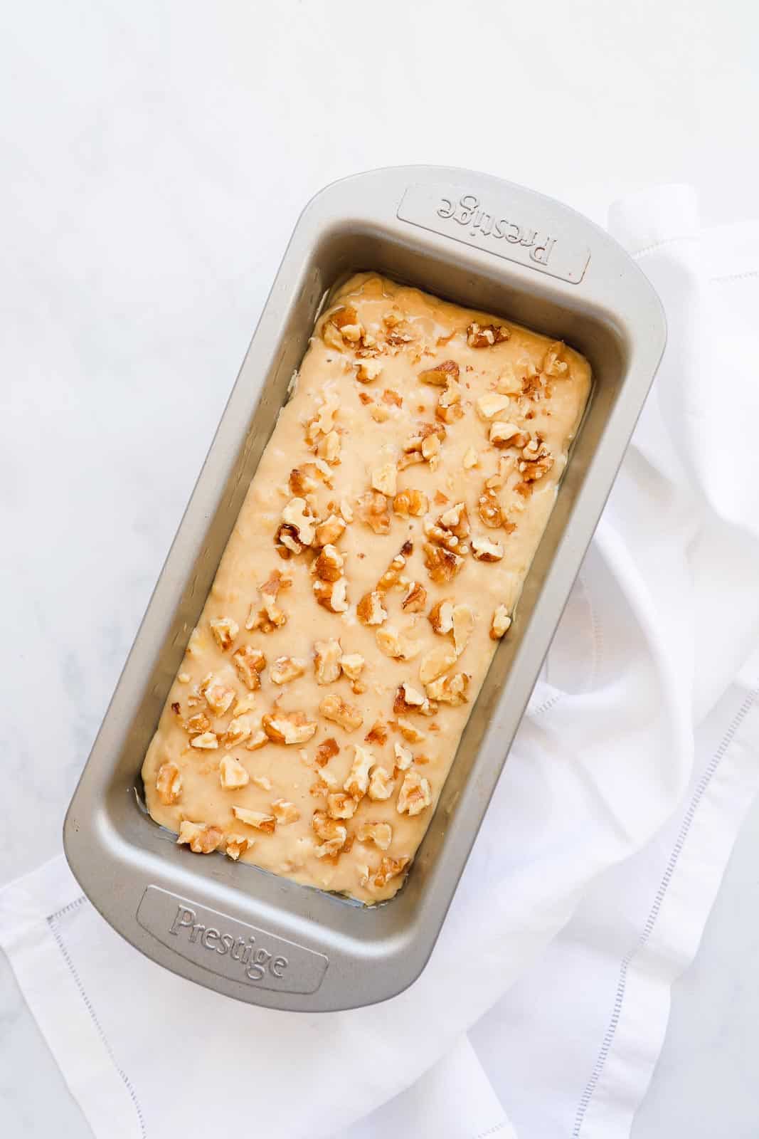 The dough in a loaf pan decorated with crushed walnuts.