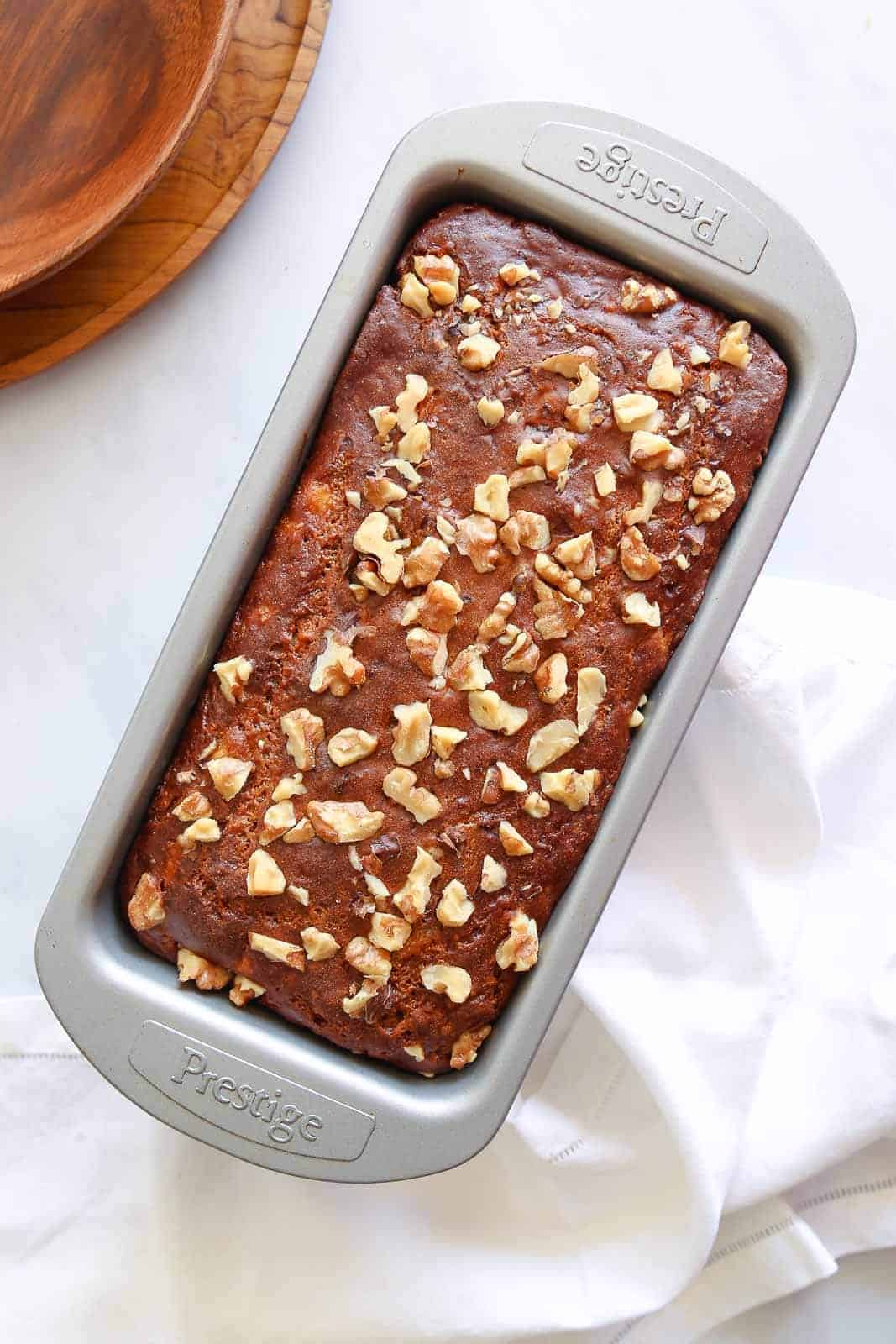 The best banana bread in a loaf baking pan topped with crushed walnuts. 