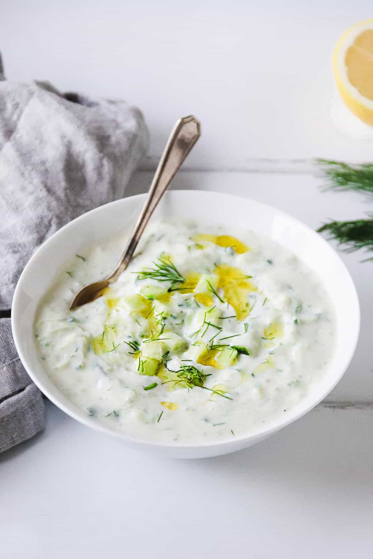 Vegan Tzatziki topped with fresh dill in a white bowl with a spoon in it. 