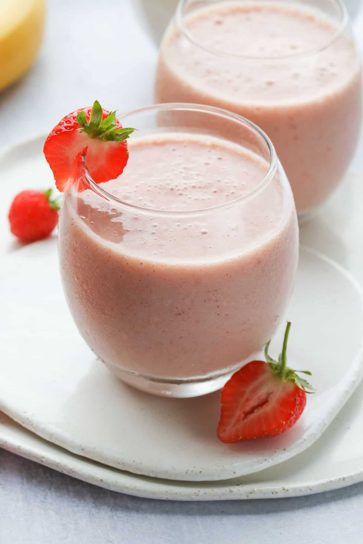 Banana strawberry smoothie served in 2 glasses, with fresh strawberries as a garnish
