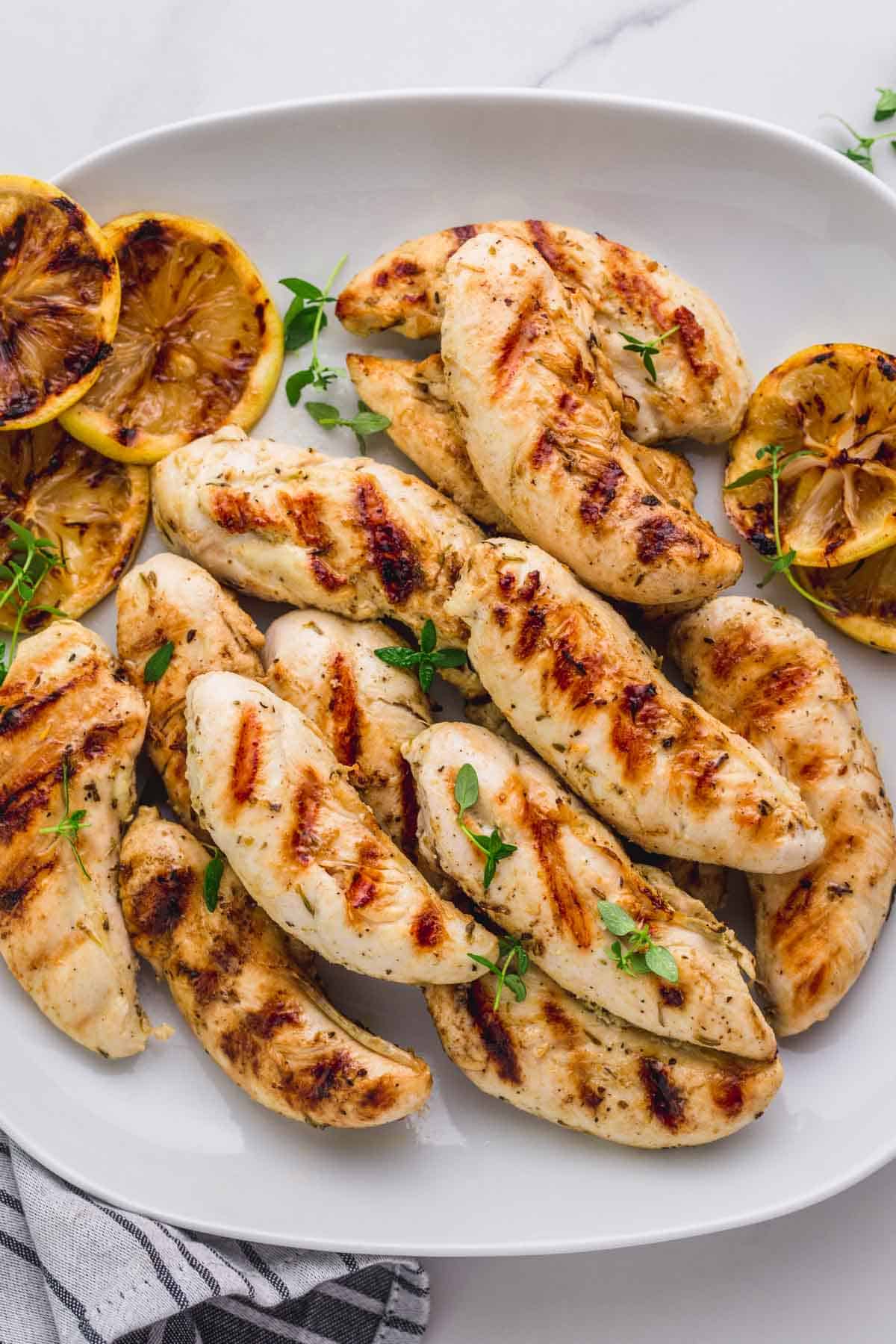 Served grilled chicken tenders in a white serving plate, with grilled lemon slices.