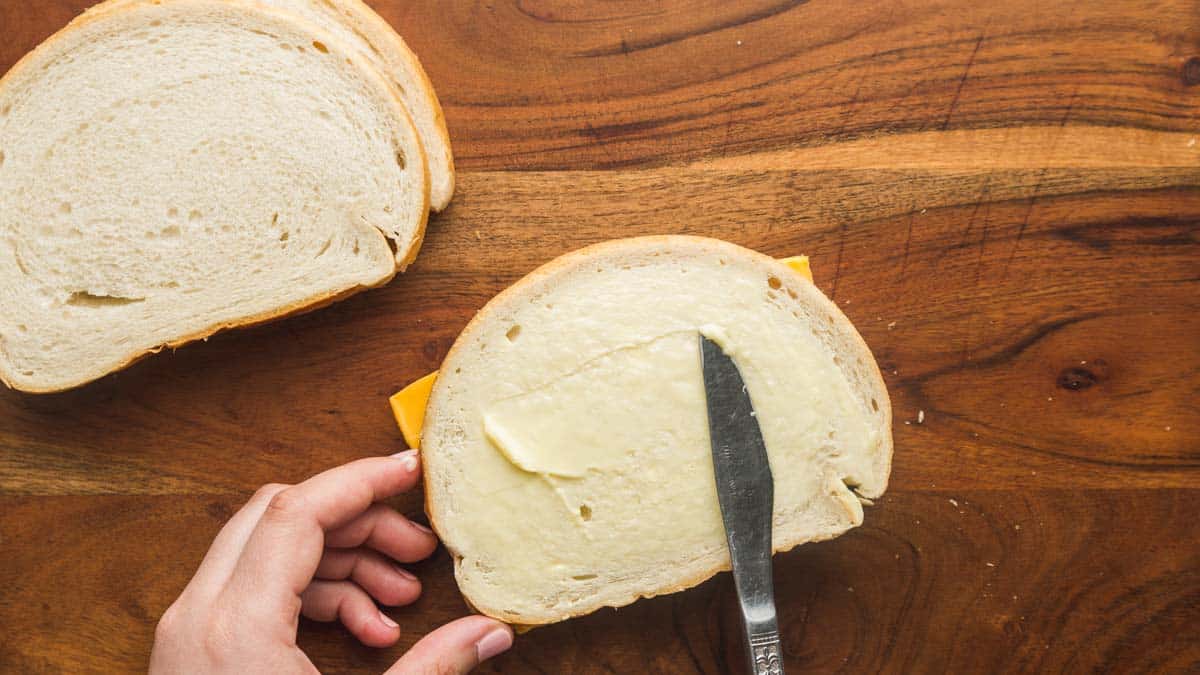 Spreading softened butter on the outside of the bread