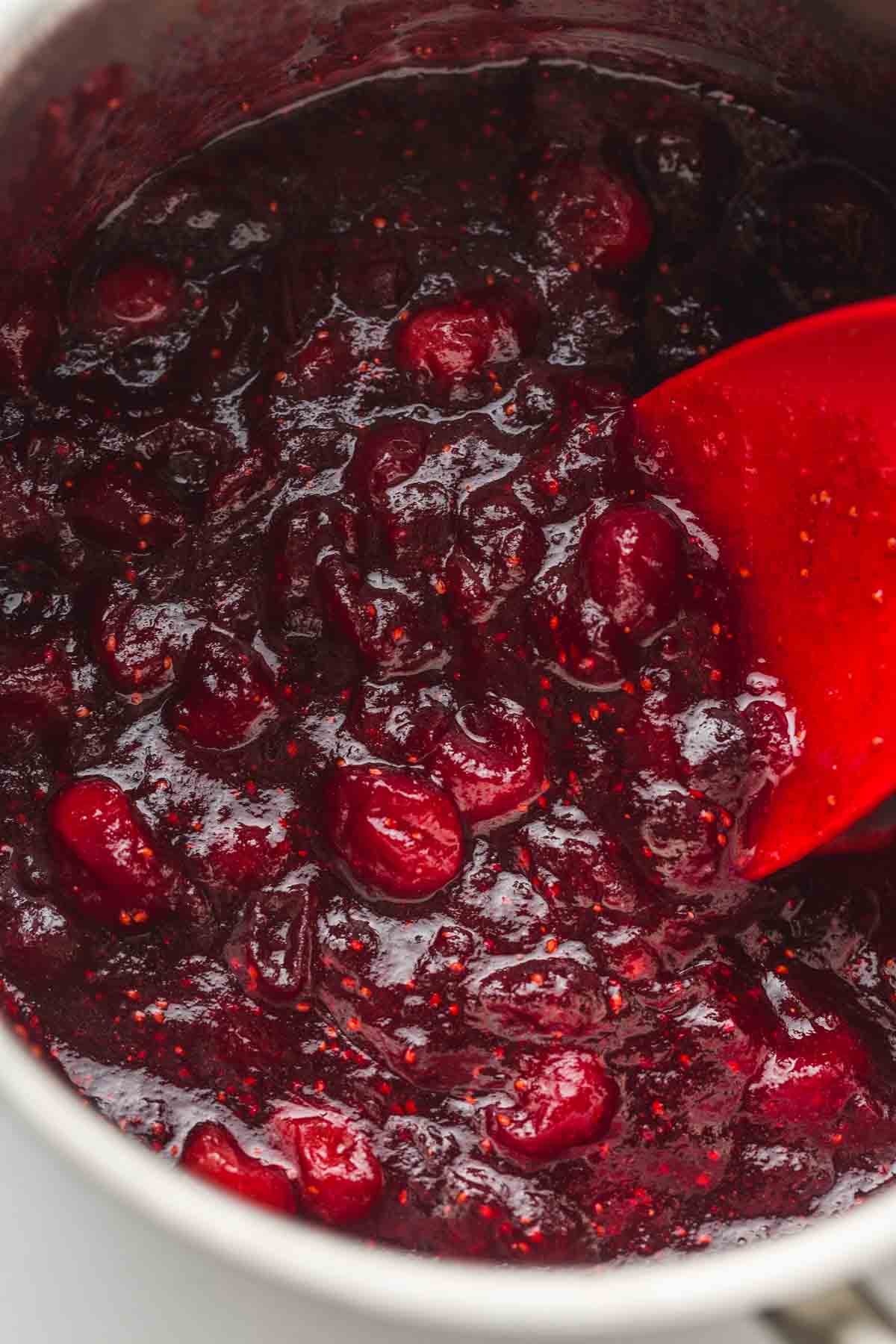 Cooking cranberries in a small saucepan with a rubber spatula
