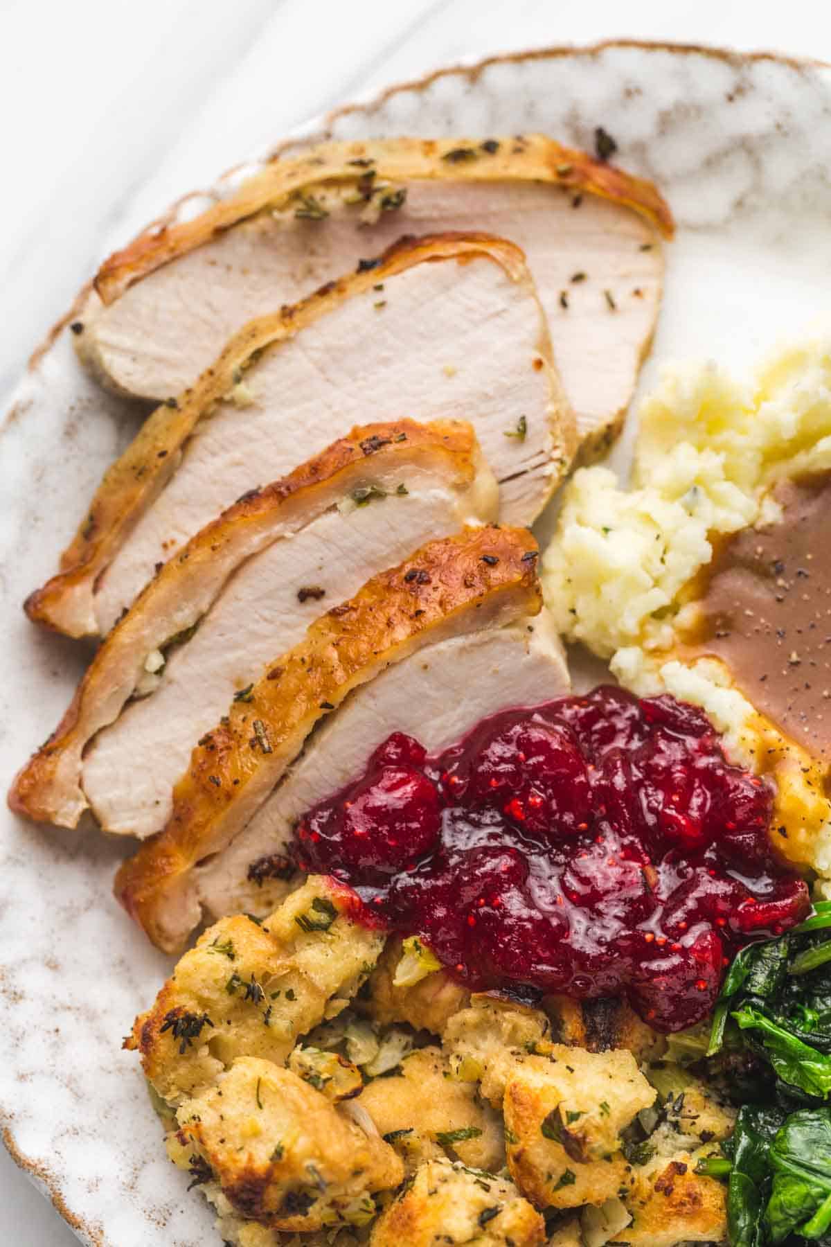 A plate with turkey slices, mashed potatoes, cranberry sauce, stuffing, and sauteed spinach