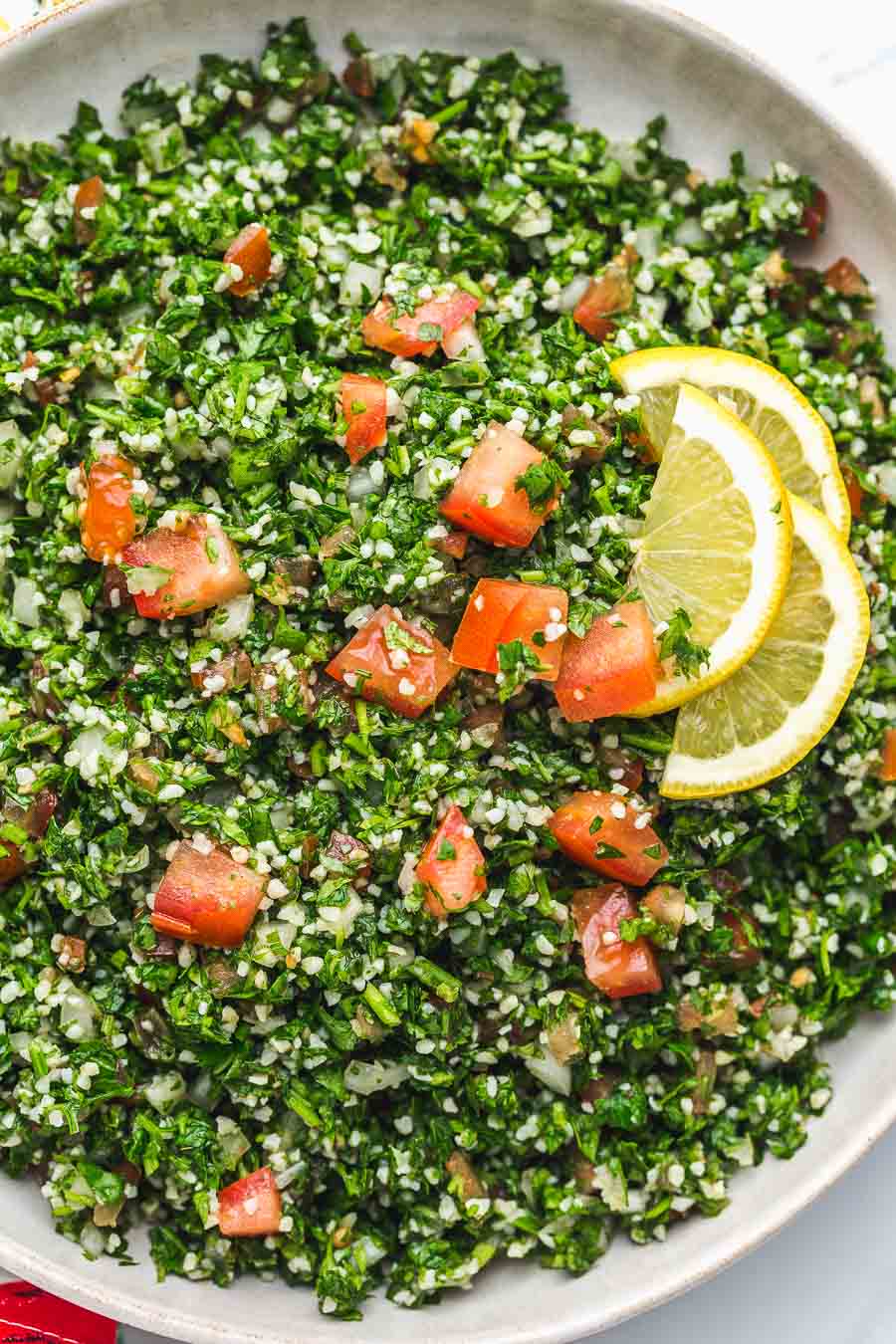 Overhead view of tabbouleh salad in a white bowl garnished with lemon slices