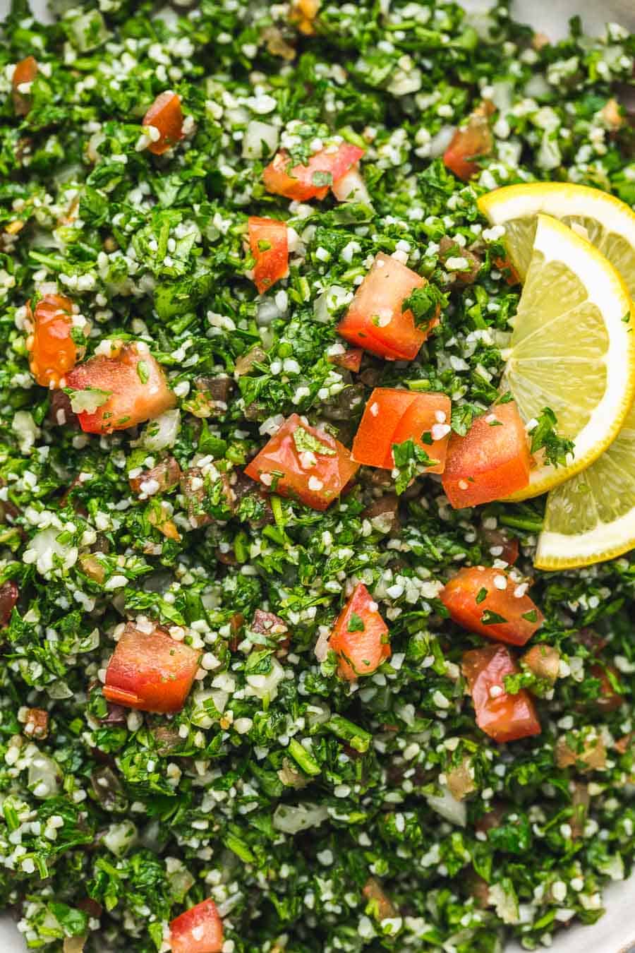 Close up of tabbouleh salad with finely chopped parsley, diced tomatoes, bulgur, and a lemon slice