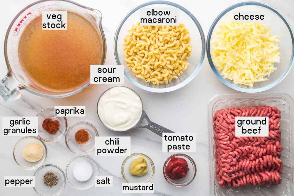 The ingredients needed for hamburger helper including ground beef, elbow macaroni, cheese, stock, sour cream, and seasonings.