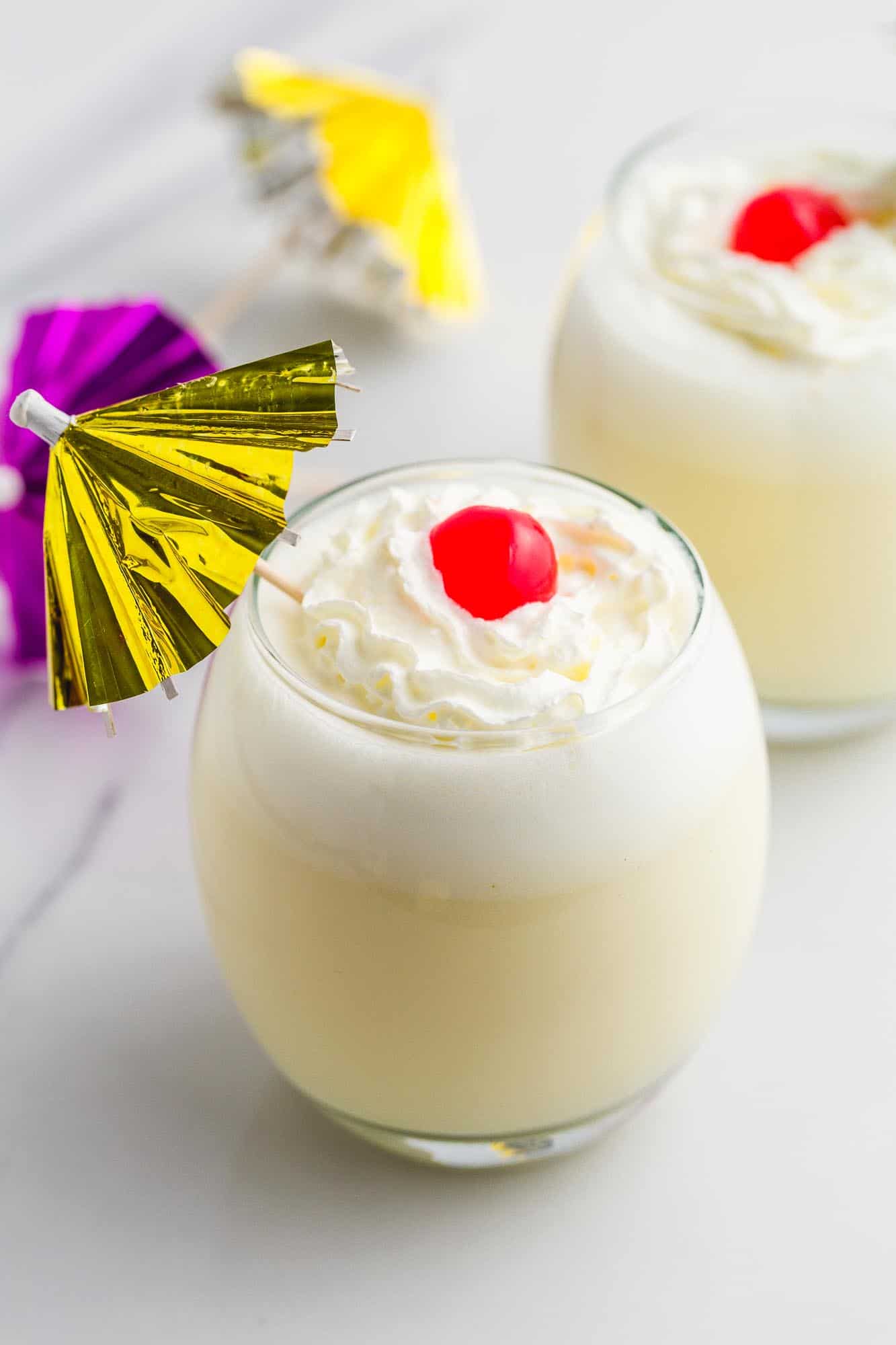 Two glasses of Piña Colada with whipped cream, maraschino cherries and cocktail umbrellas