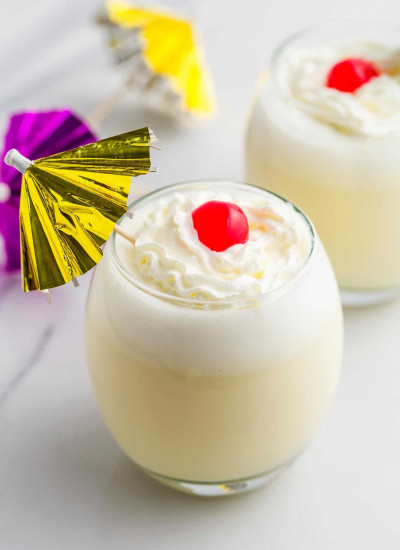 Piña Colada in 2 glasses with whipped cream and maraschino cherries, and cocktail umbrellas