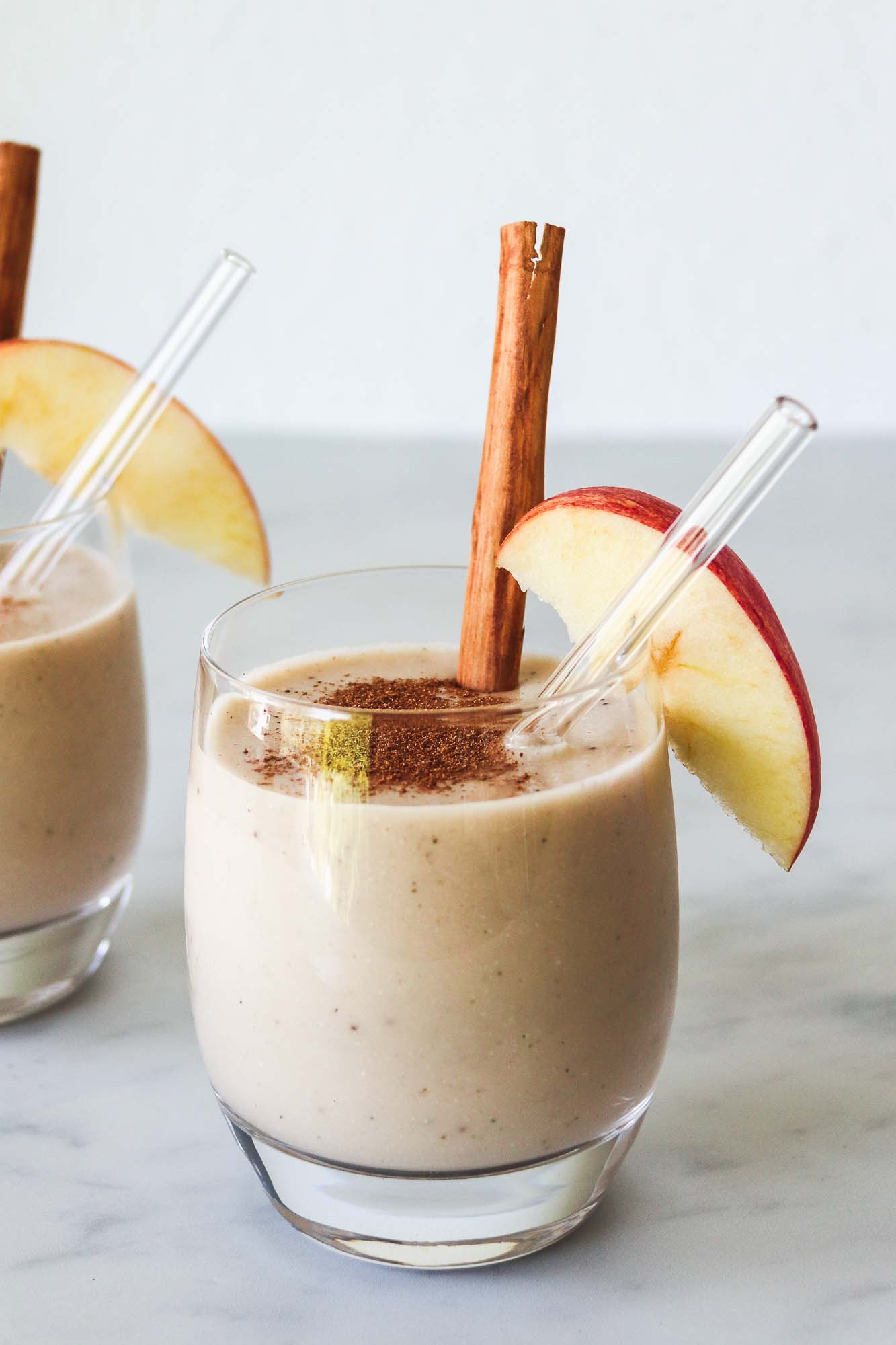 Apple and banana smoothie poured into two glasses and decorated with apple slices and cinnamon. 