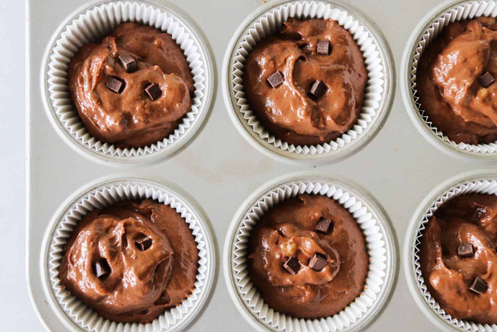 Overhead shot of chocolate banana muffin batter scoops in a muffin tin, topped with chocolate chunks