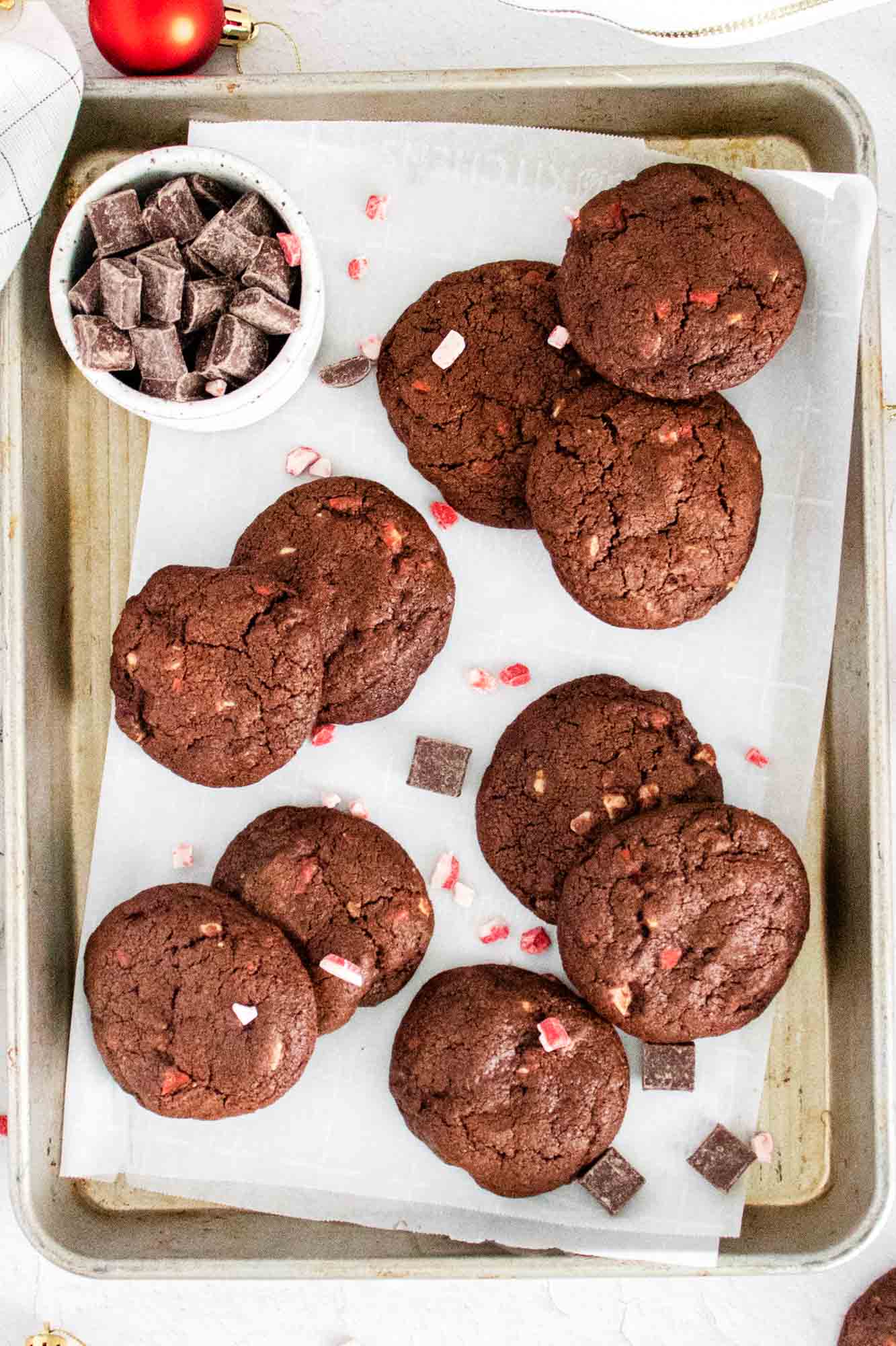 Overhead shot of Chocolate Peppermint Cookies placed on parchment paper, and chocolate chunks in a bowl on the side.