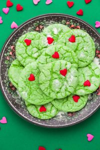 Overhead shot of grinch cookies on a plate, with heart sprinkles on the sides