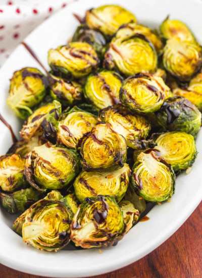 A white oval plate with roasted brussels sprouts and balsamic glaze