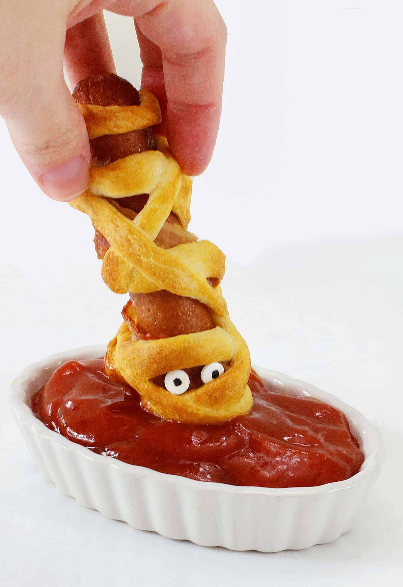 Dipping a mummy hot dog in ketchup