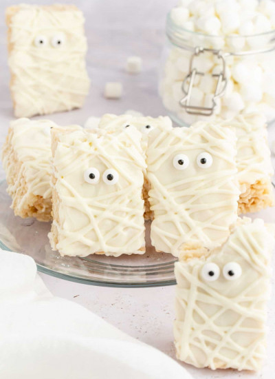 Mummy Rice Krispie Treats with candy eyes, standing on a glass plate.