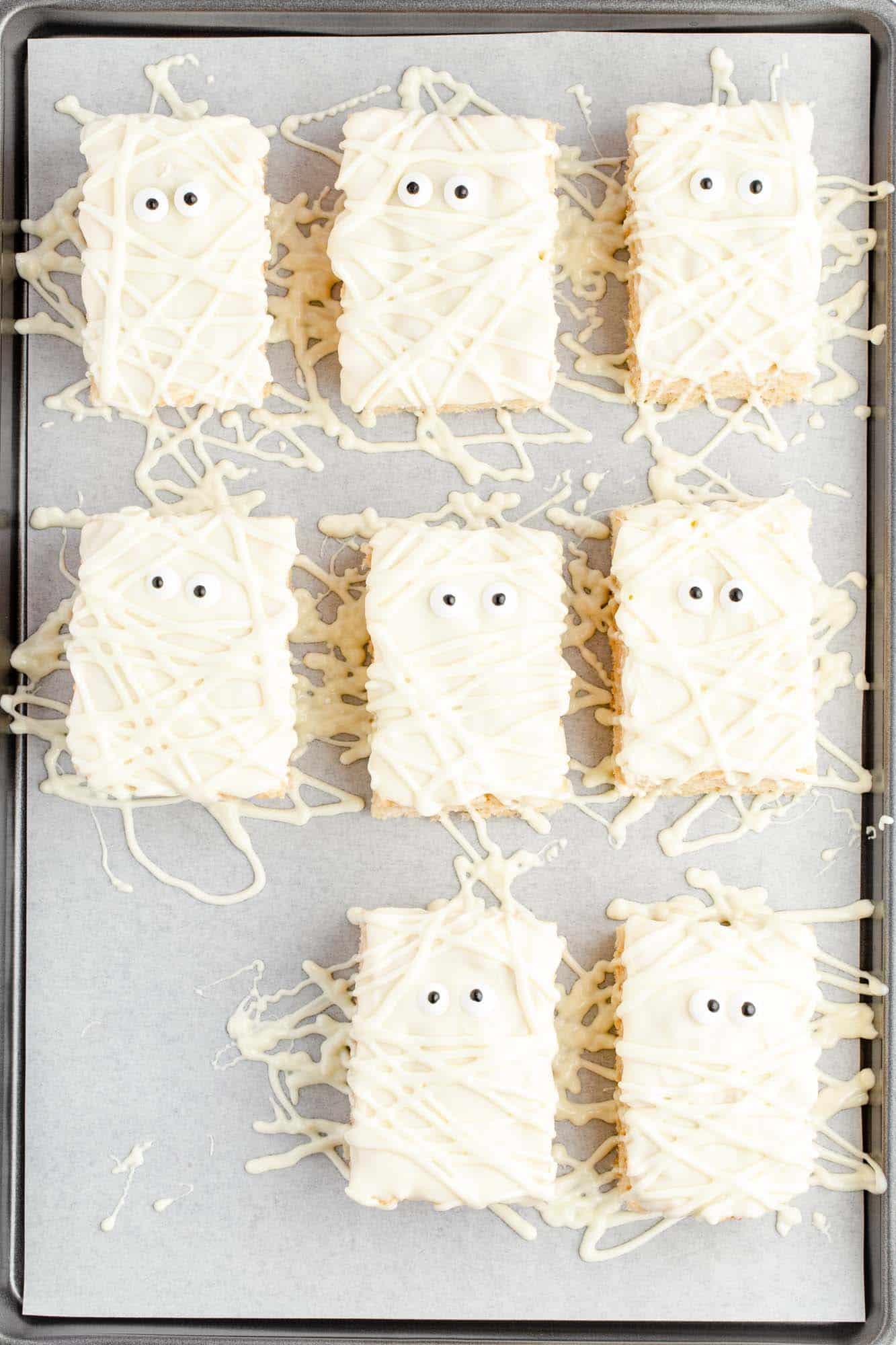 Overhead shot of rice krispie treats that are decorated to look like mummies, placed on a cookie sheet lined with parchment paper.