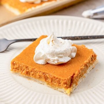 A slice of pumpkin slab pie on a white plate, with whipped cream on top
