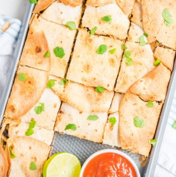 Overhead shot of sheet pan quesadillas with a small bowl of salsa, and a half of a lime.