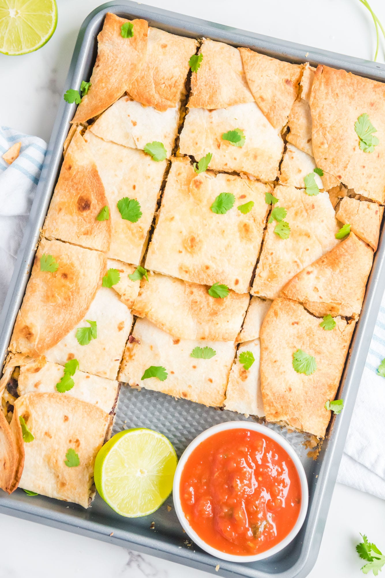 Overhead shot of sheet pan quesadillas with a small bowl of salsa, and a half of a lime.