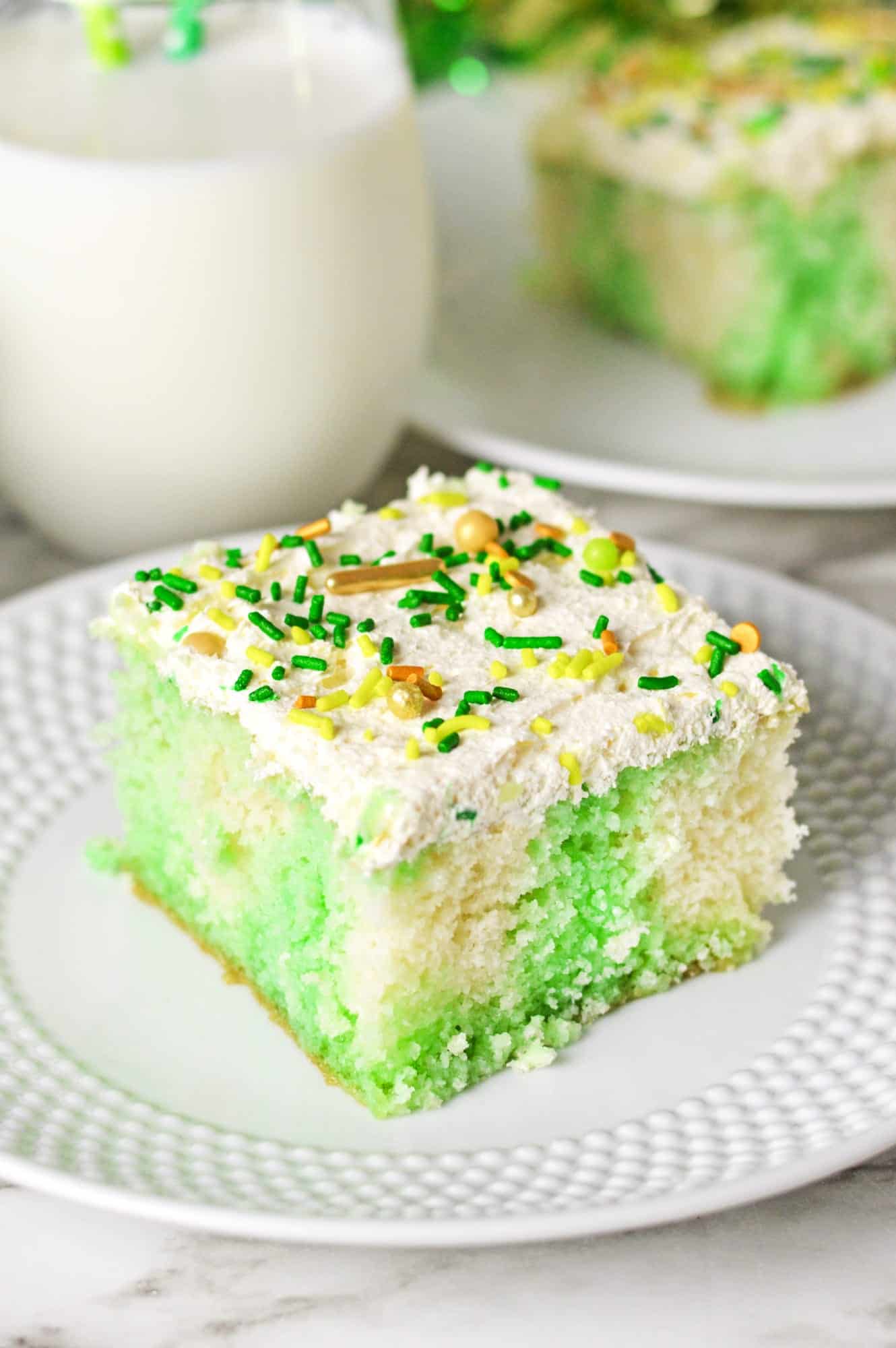 A slice of lime jello poke cake on a small white plate, decorated with St. patrick's day sprinkles.
