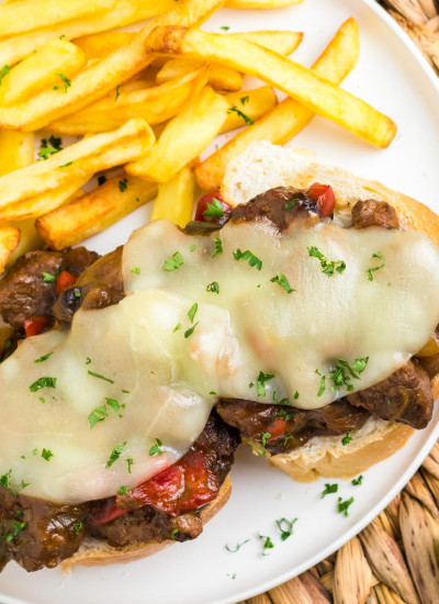 Philly cheesesteak on bread as an open face sandwich, with fries on the side.