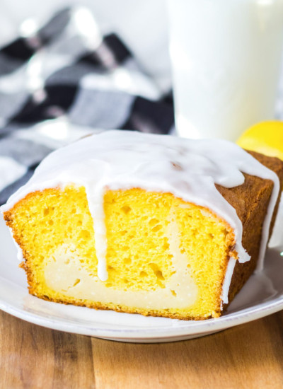 Lemon cheesecake loaf cake with the icing dripping off, placed on a white plate, with a glass of milk in the background.