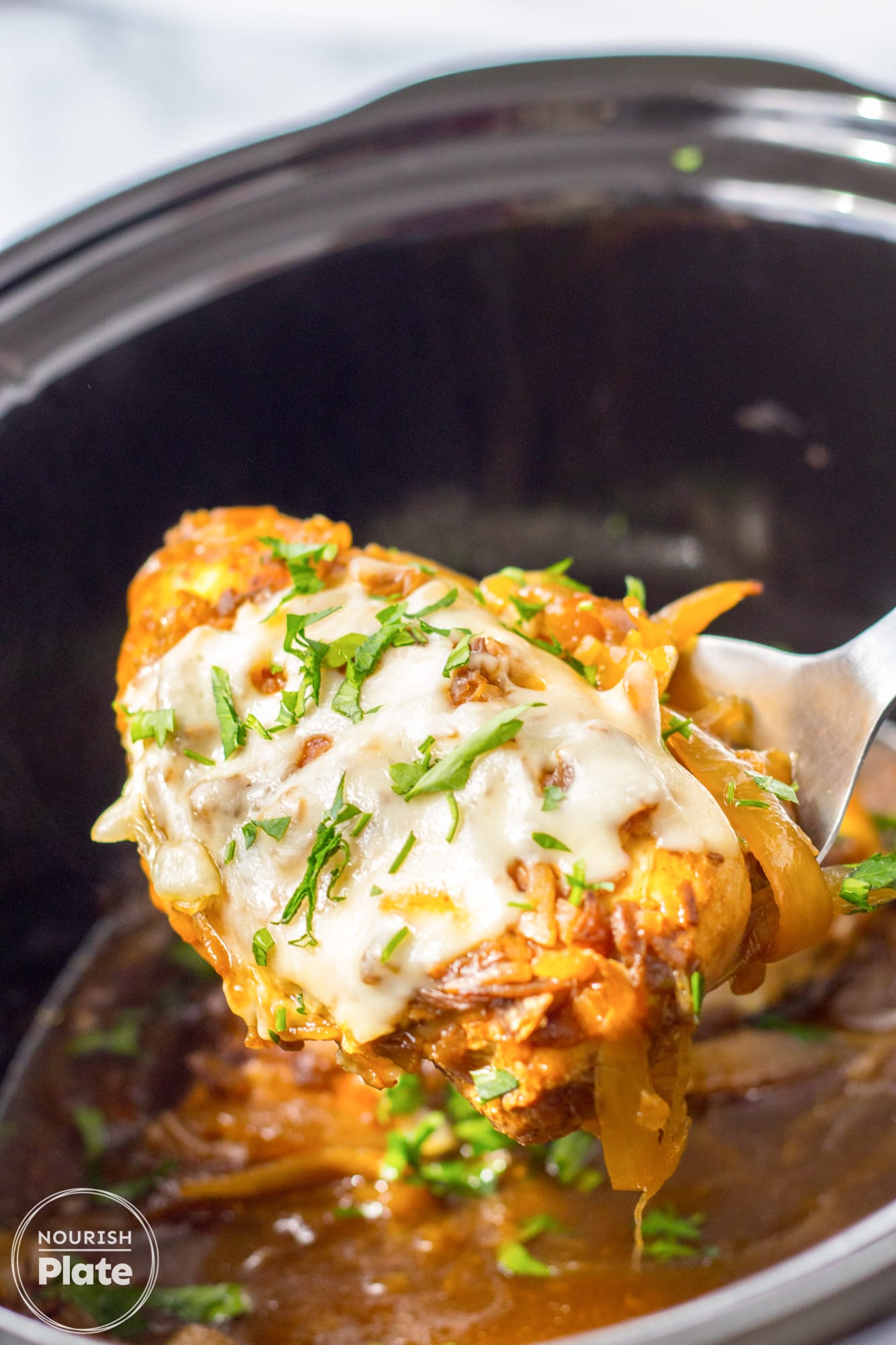 French onion chicken with cheese being serving with a serving spoon from a crockpot