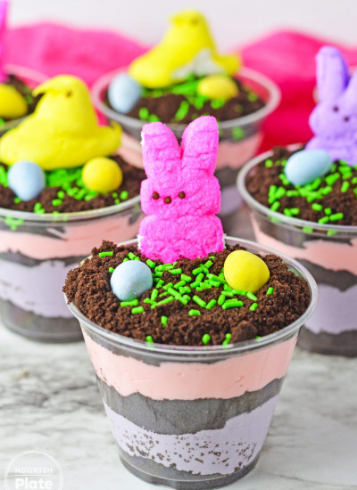 Easter dirt cups with layered instant pudding in colors, topped with peeps and mini eggs.