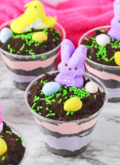 Easter dirt cups with layered instant pudding in colors, topped with peeps and mini eggs.