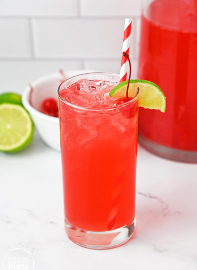 A glass filled with vibrant cherry limeade and ice, garnished with a slice of lime, and a straw.
