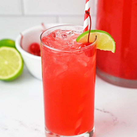 A glass filled with vibrant cherry limeade and ice, garnished with a slice of lime, and a straw.