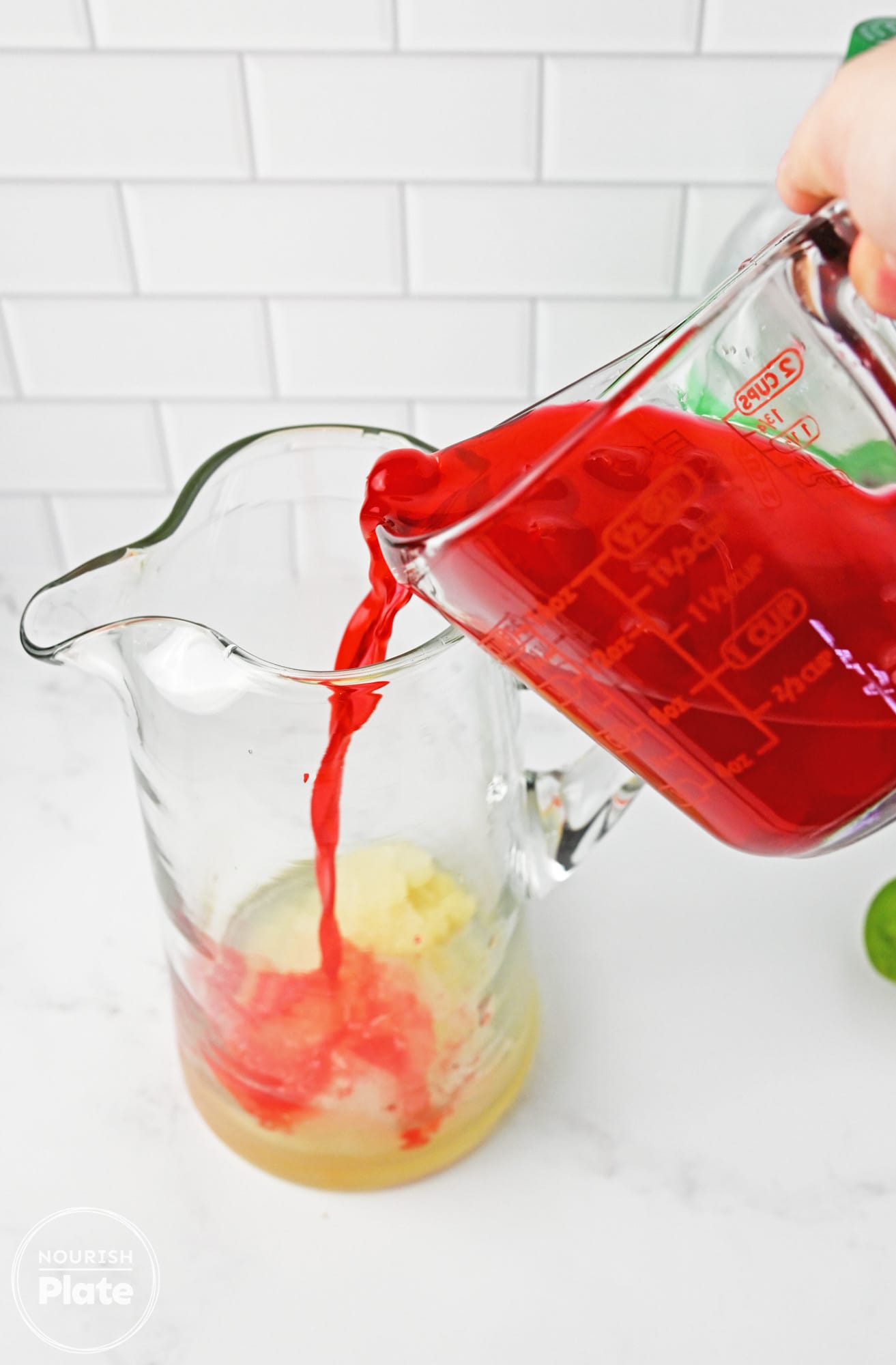 Pouring maraschino cherry juice over frozen lemonade in a pitcher