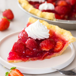 A slice of fresh strawberry pie on a small white plate, with whipped cream on top