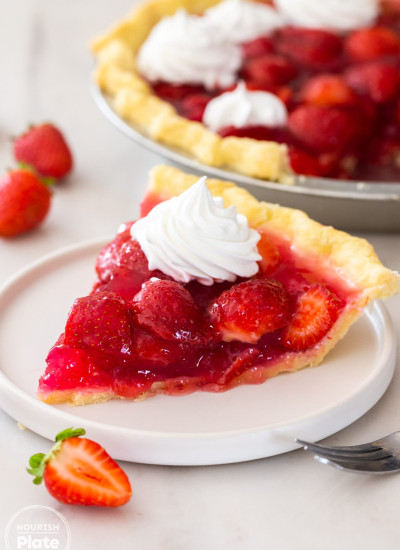A slice of fresh strawberry pie on a small white plate, with whipped cream on top