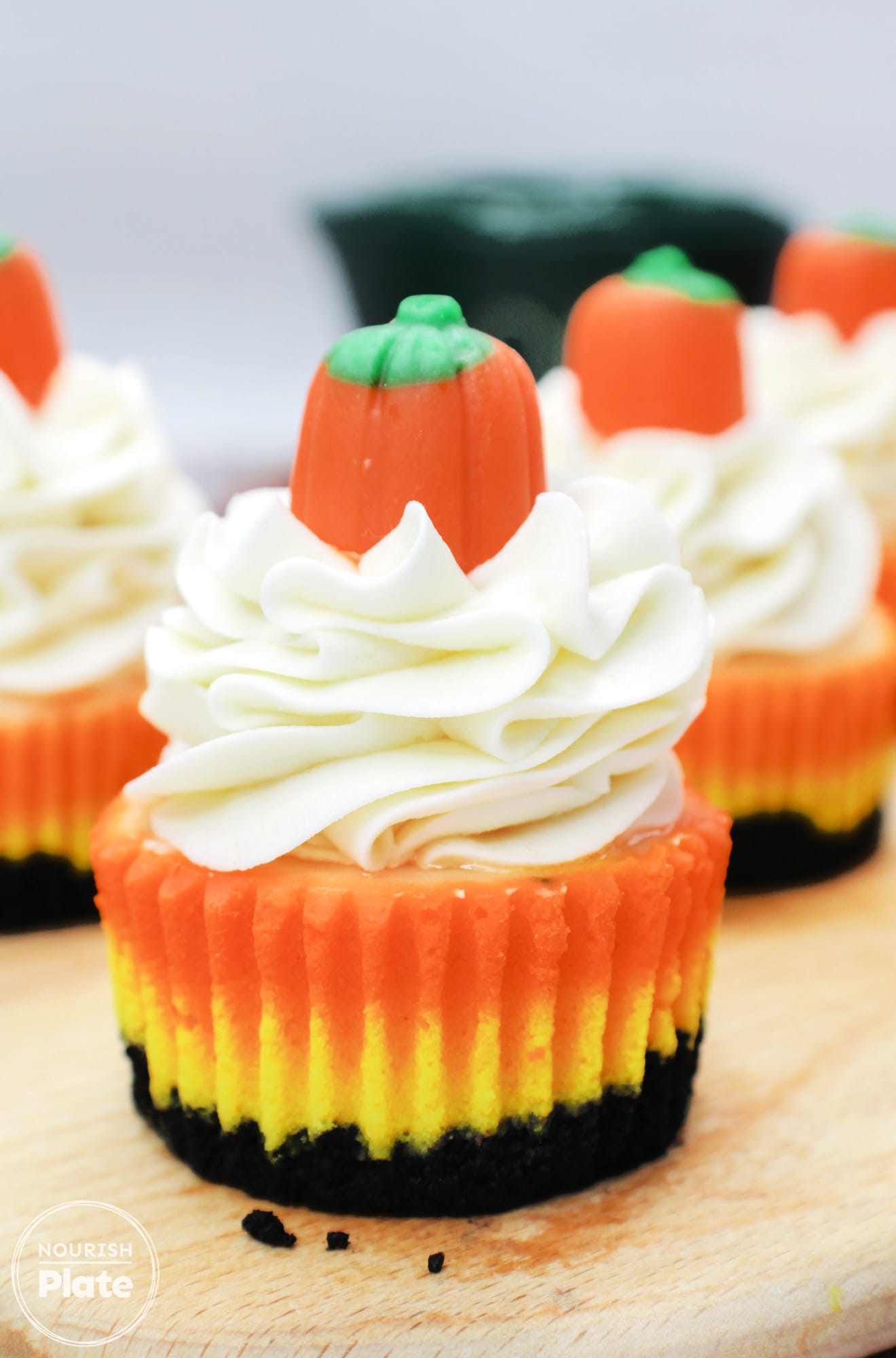 Mini candy corn cheesecake topped with whipped cream and a candy pumpkin