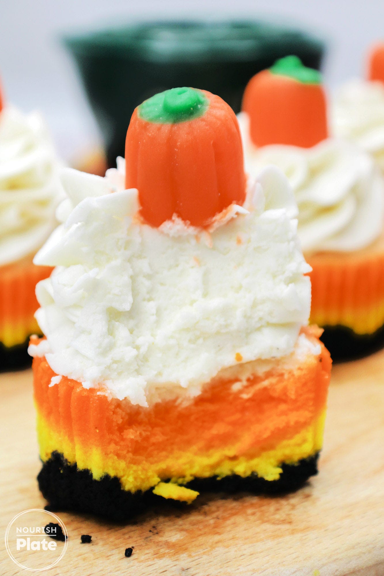 A bite shot of a candy corn mini cheesecake topped with whipped cream and candy pumpkin