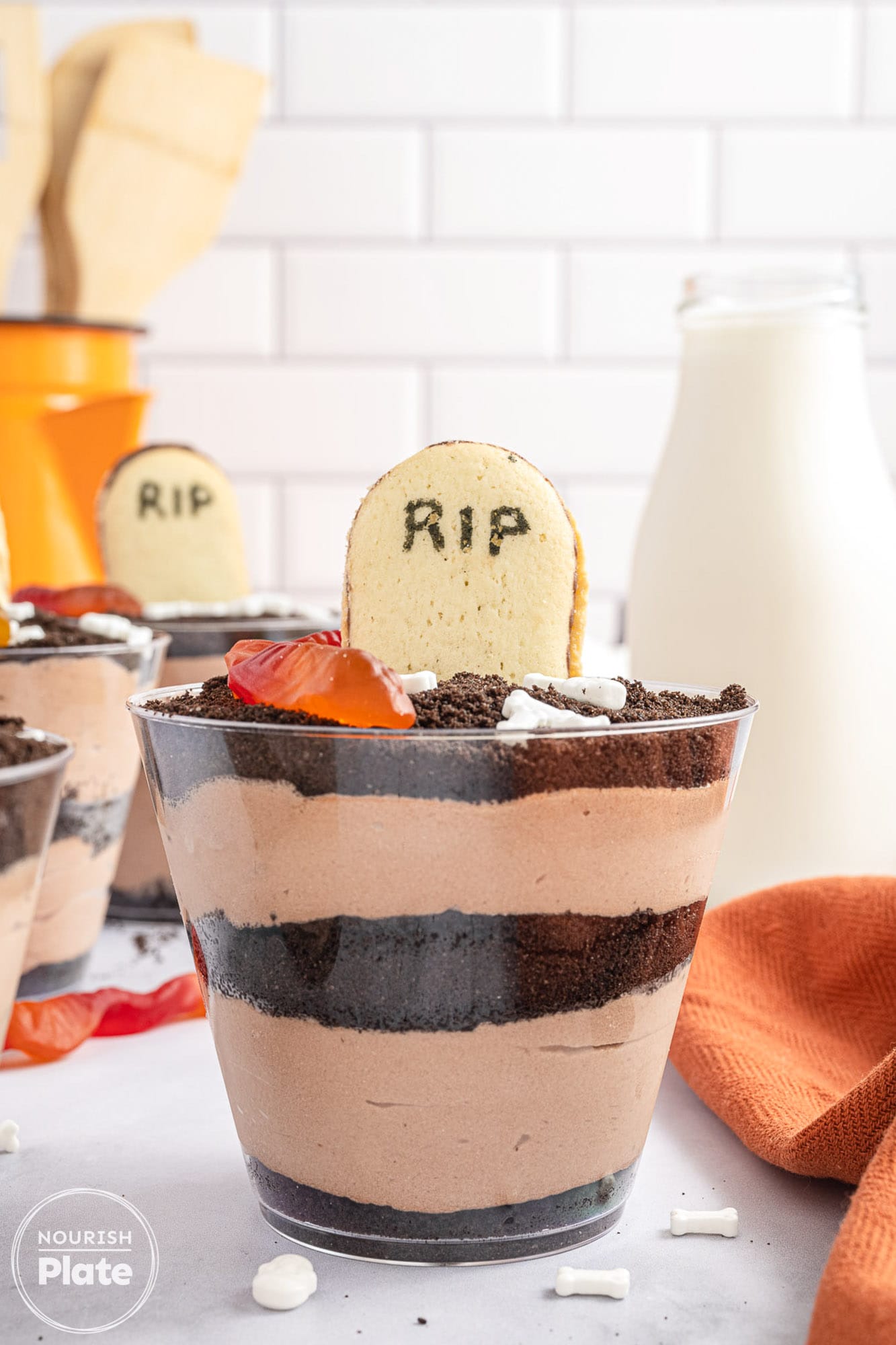 A dirt cups of layers of chocolate pudding and oreo crumbs, decorated with a milano cookie to look like a tombstone