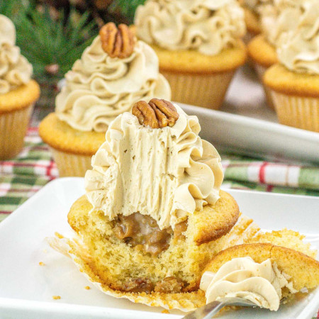 Pecan pie cupcakes on a white plate, showing a bite shot to expose the pecan pie filling and a fork on the side.