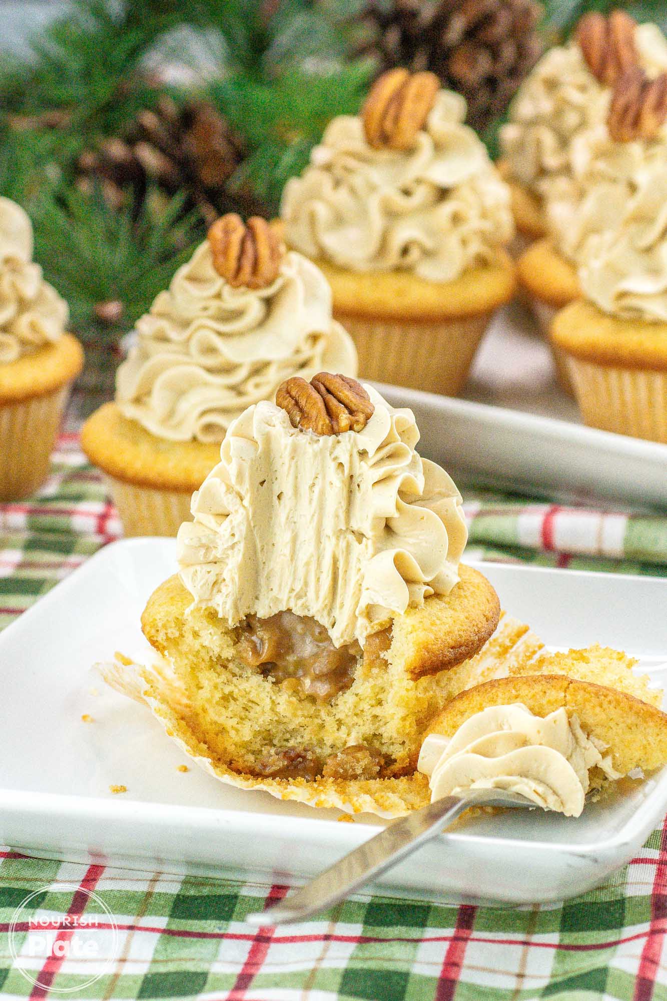 Pecan pie cupcakes on a white plate, showing a bite shot to expose the pecan pie filling and a fork on the side.