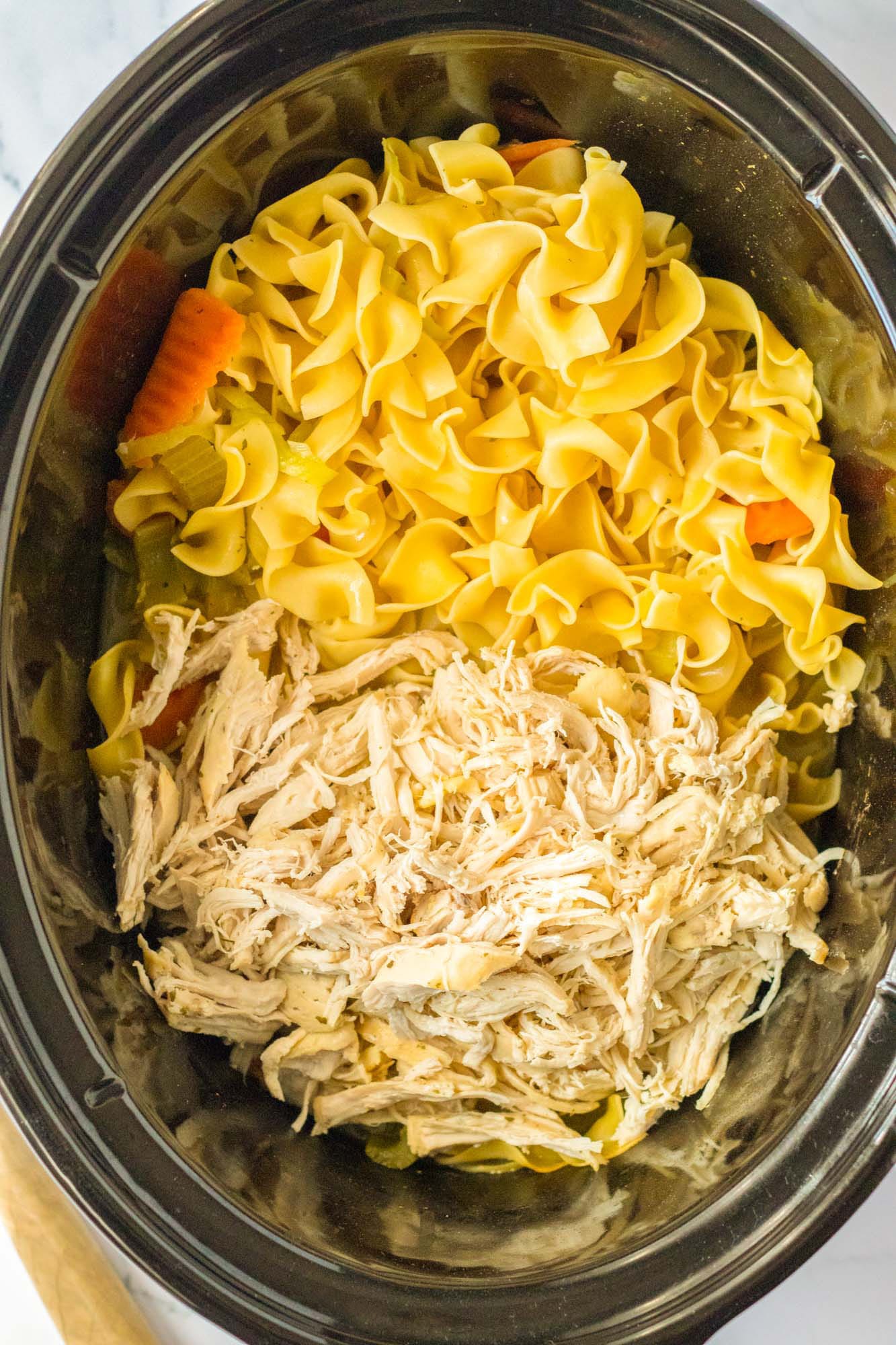 Overhead shot of noodles and shredded chicken in a crockpot