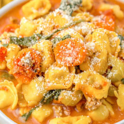 Angle shot of tortellini soup with sausage in a white bowl