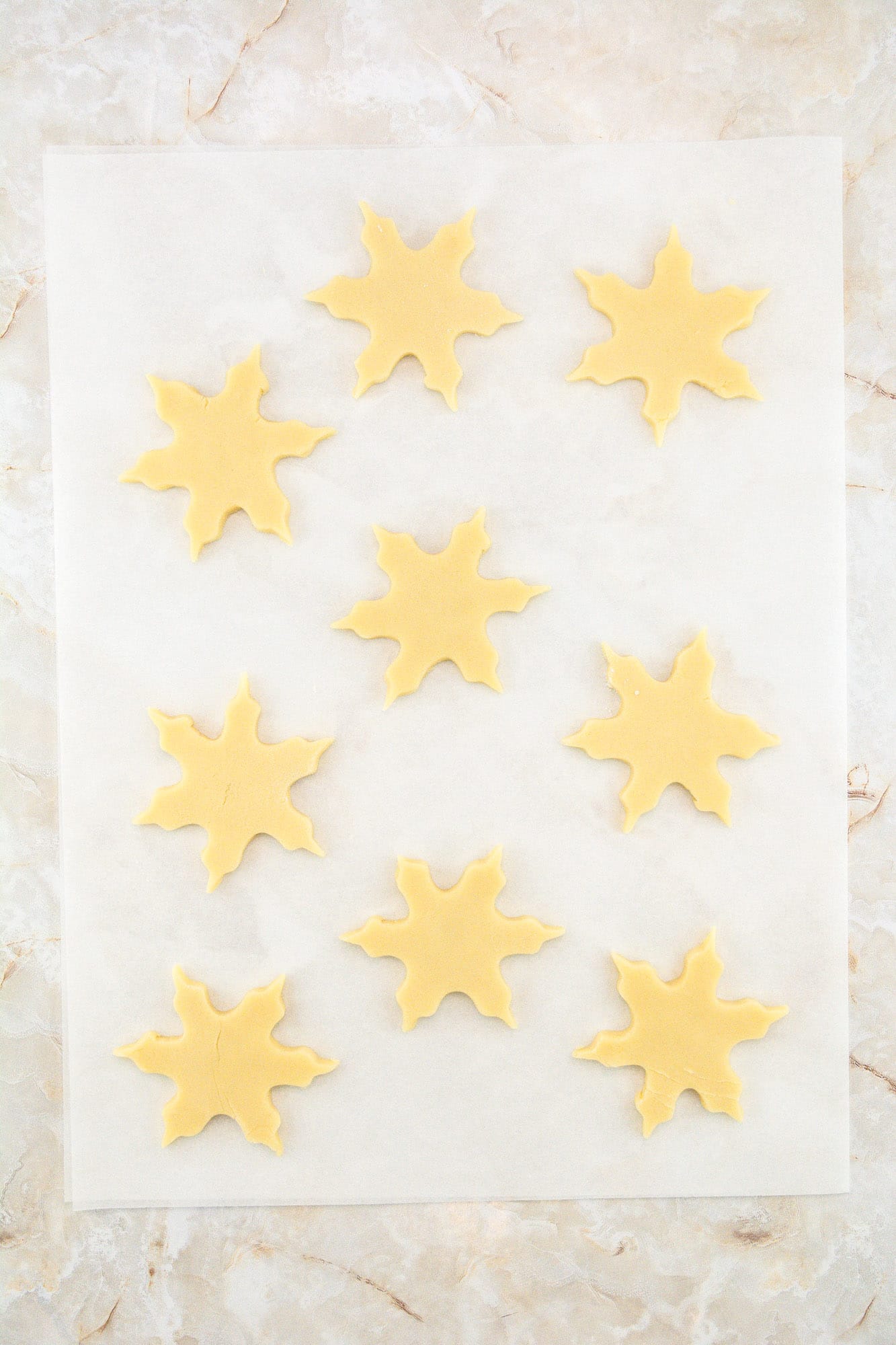 Snowflake shaped cut out cookies placed on parchment paper