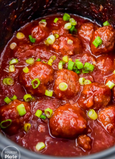 Cranberry meatballs in sauce in the slow cooker garnished with sliced green onions