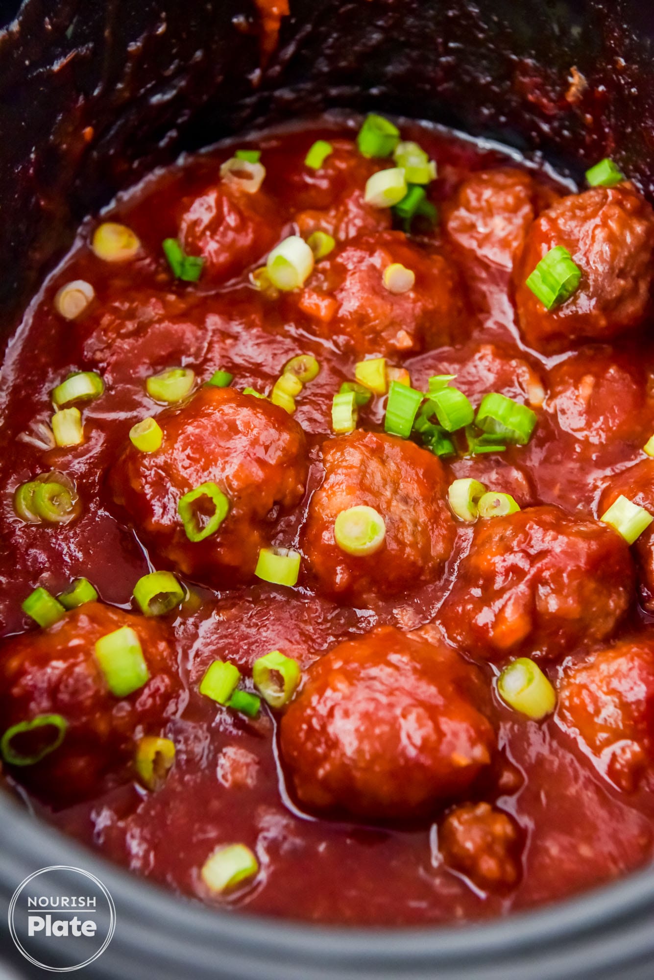 Spicy cranberry meatballs in the slow cooker, garnished with sliced green onions.