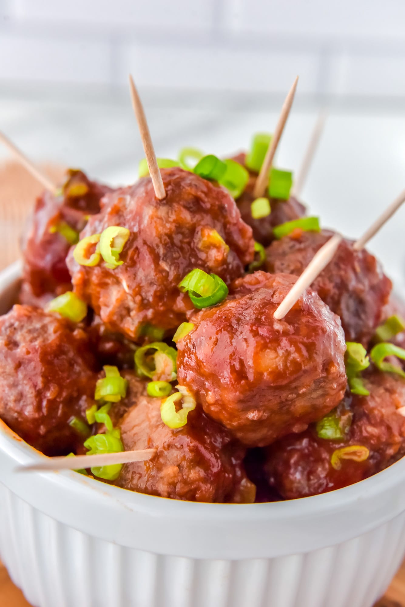 Cranberry meatballs with toothpicks inserted, and garnished with sliced green onions. Served in a white dish.
