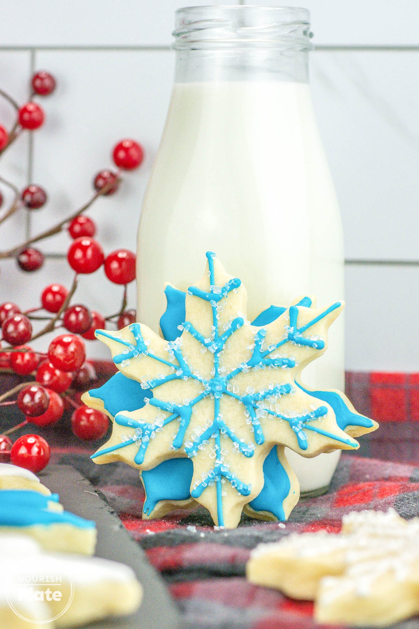 2 snowflake shaped cookies decorated with white and blue icing, and a glass bottle with milk in the background