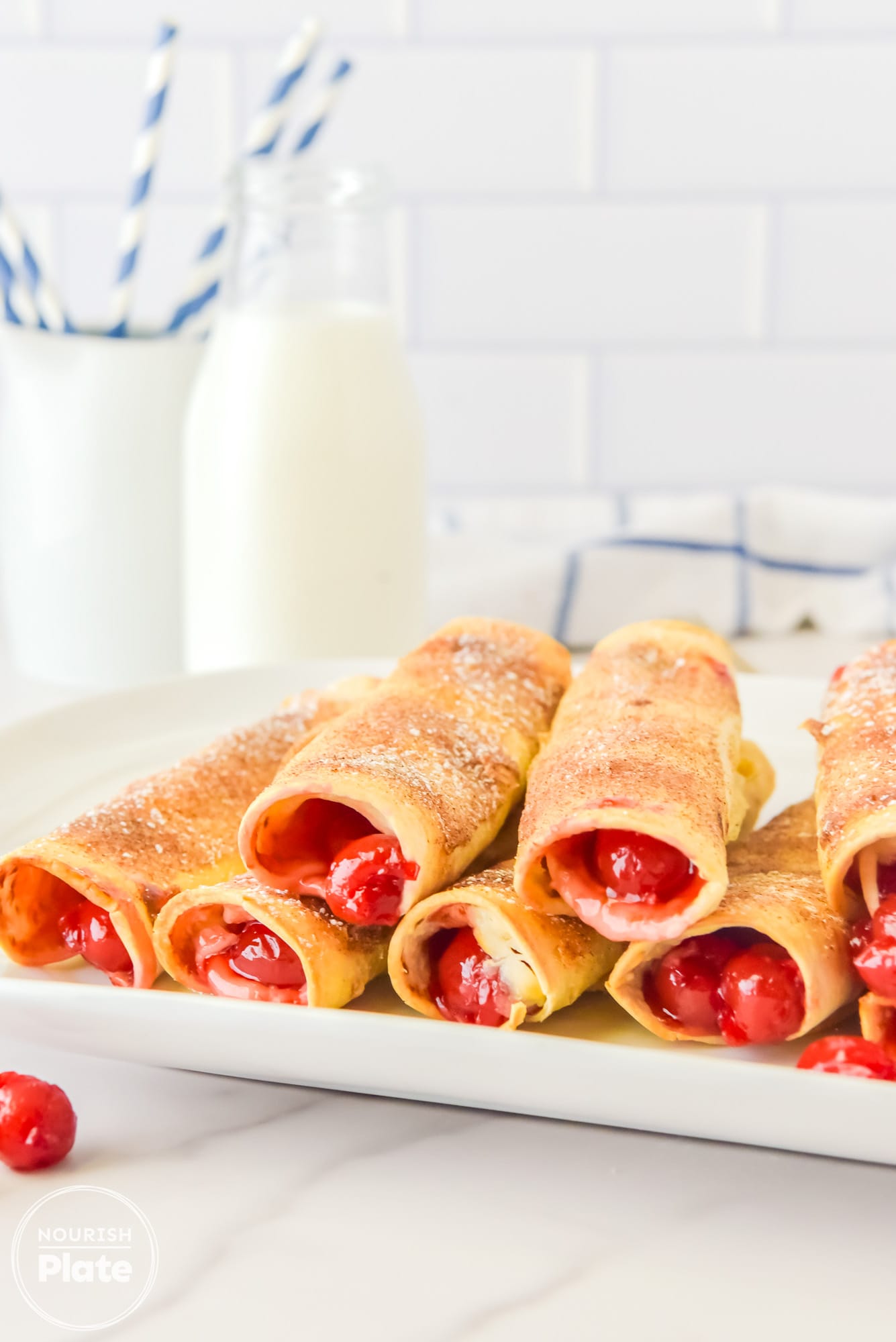 Stacked Cherry Cheesecake Taquitos on a plate, with a glass of milk in the background