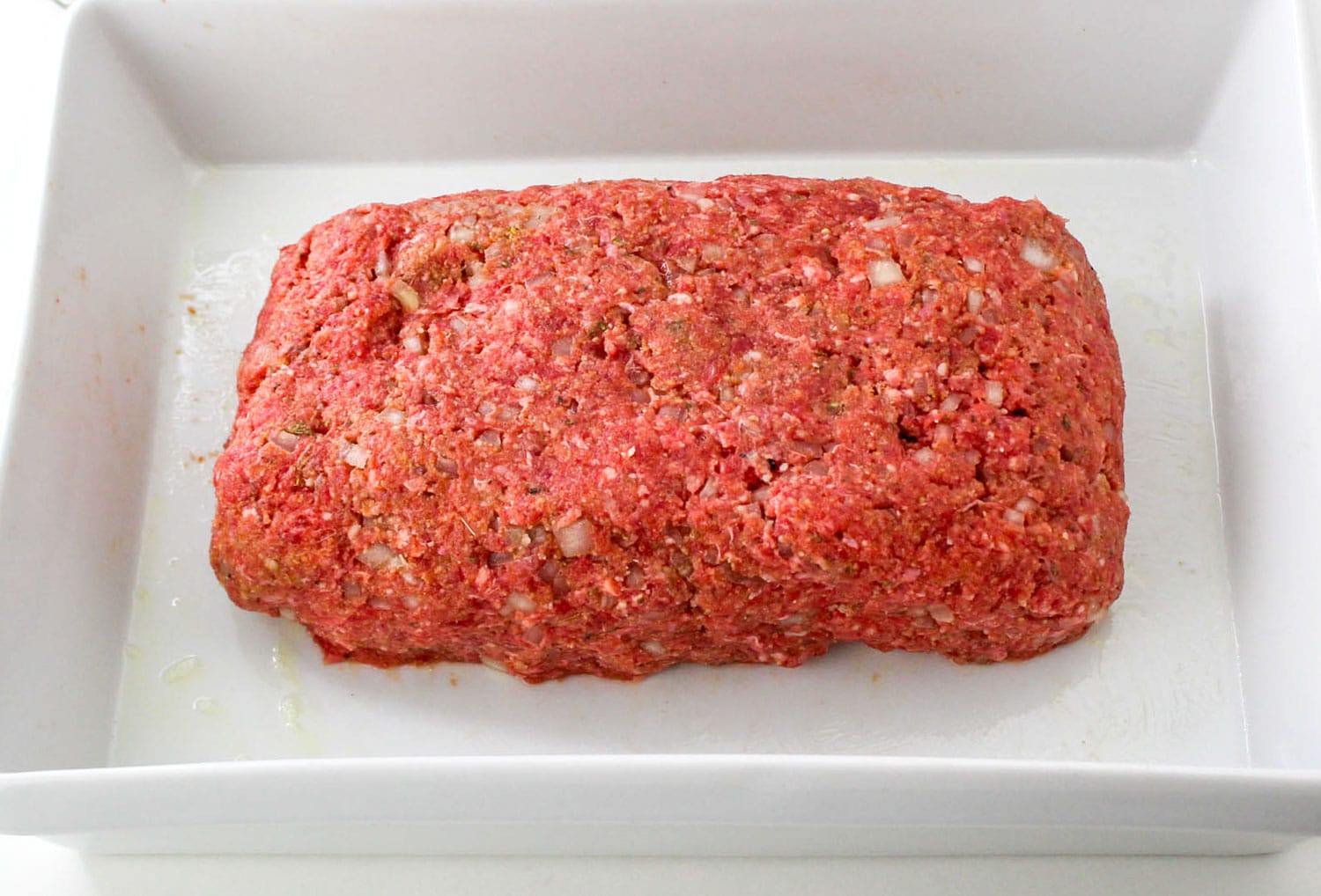 Raw meatloaf shaped and placed in a white baking pan