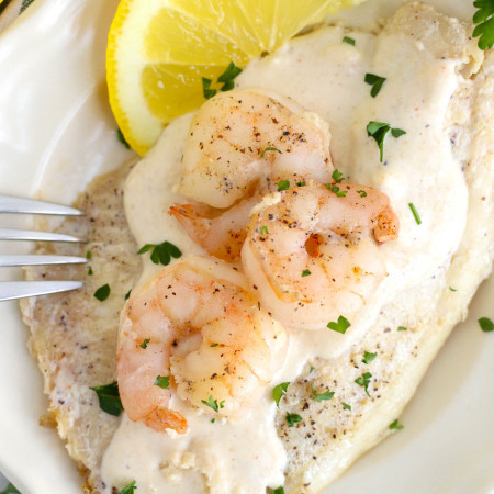 Pan Seared Tilapia and Shrimp on a plate, with a creamy sauce, and fresh lemon slices